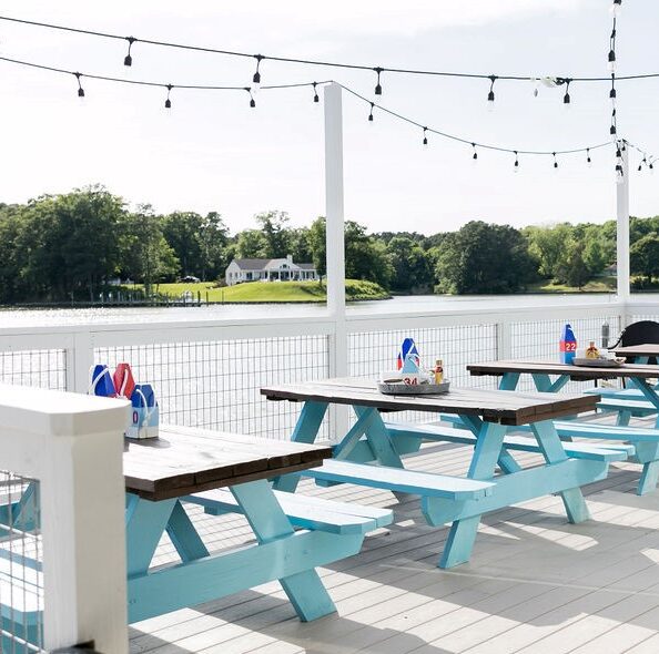 an outdoor patio with string lights and light blue picnic tables looking out of the water