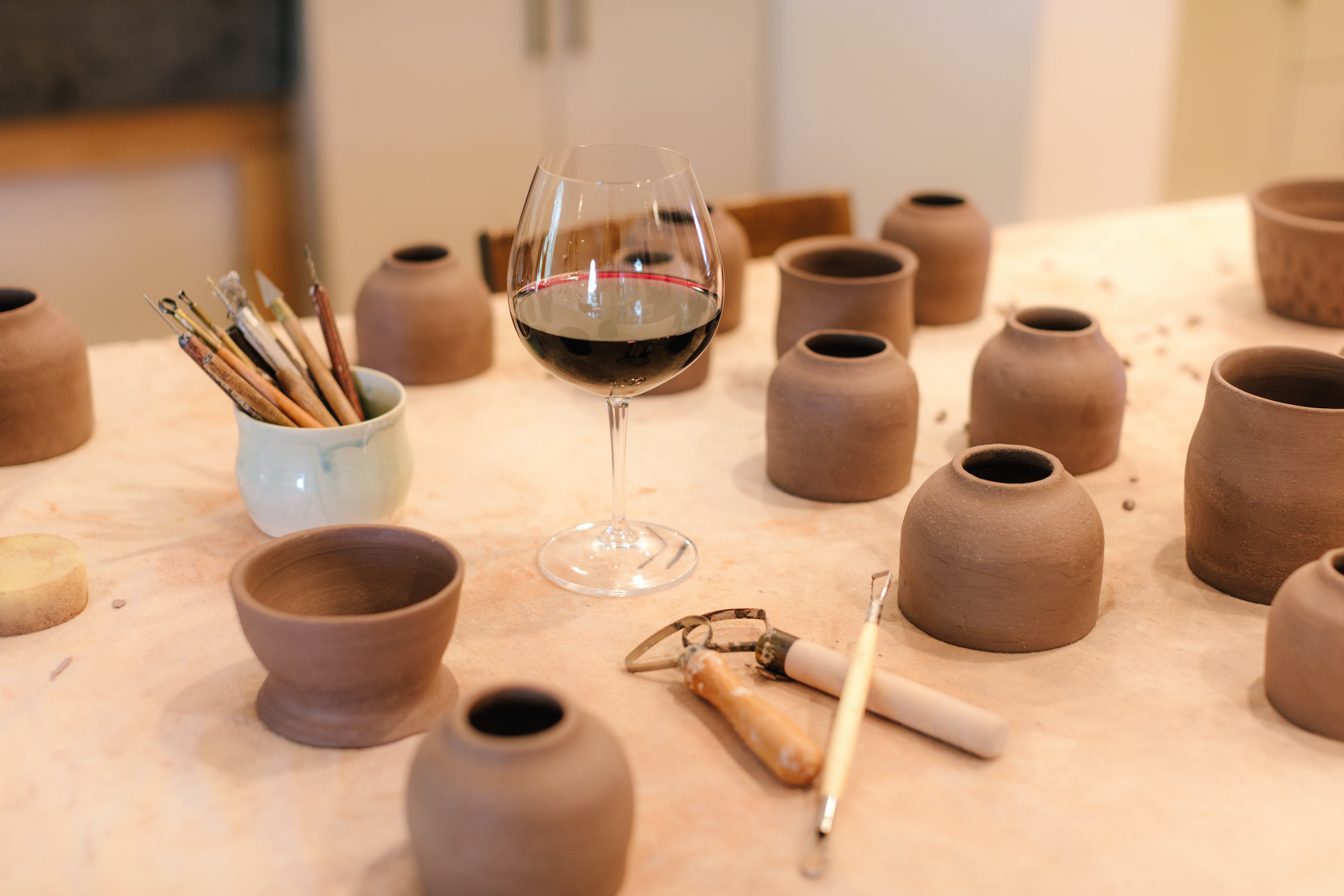 a table with several small, un-fired pots and a glass of wine
