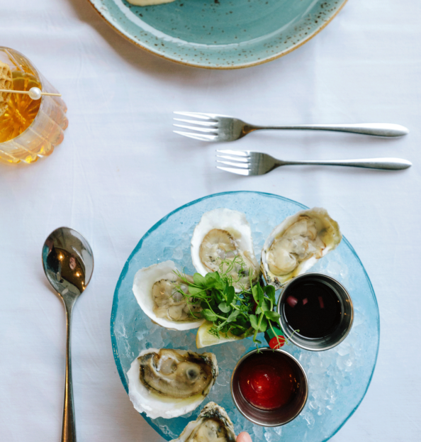 A table with a white table cloth, and a glass bowl full of ice and oysters with two sauces