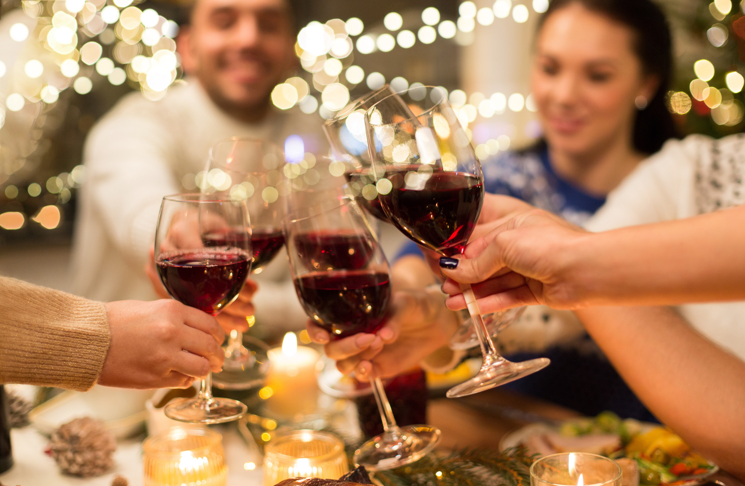 close up of happy friends having christmas dinner at home, drinking red wine and clinking glasses